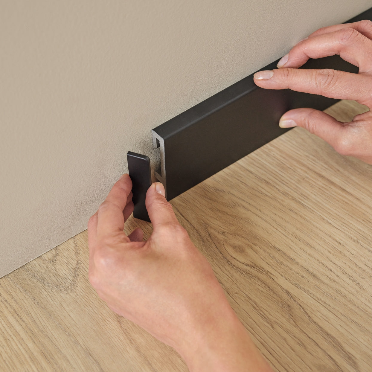 A lifestyle image of the Black Vox Espumo skirting boards. The image shows a person applying the matching cover cap.